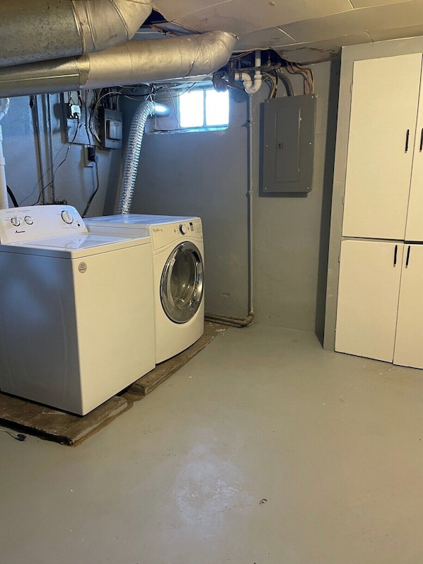 A laundry room with a front-loading washer and dryer, ductwork, and a utility cabinet.