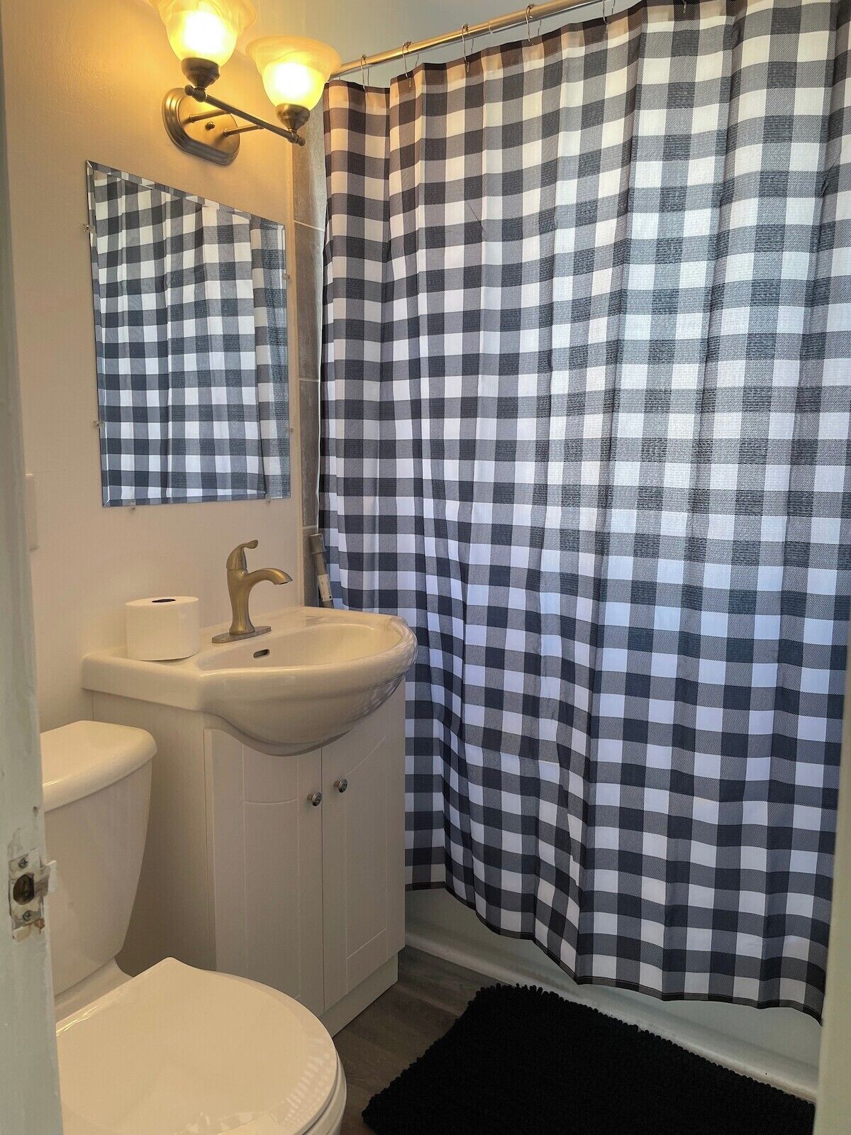Un baño con cortina de ducha a cuadros, un lavabo con espejo y un inodoro.
