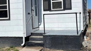 Una pequeña casa de un piso con techo de tejas grises, fachada blanca y ventana con marco negro.