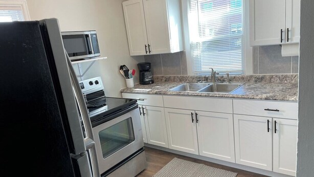 Una cocina con gabinetes blancos, un refrigerador de acero inoxidable, un microondas, una estufa y un lavamanos.