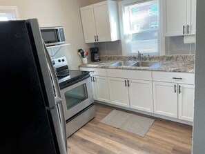 A kitchen with white cabinets, a stainless steel refrigerator, a microwave, a stove, and a sink.