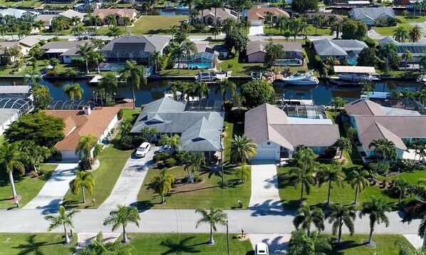 Vista aérea de uma área residencial com casas, palmeiras e um corpo d'água.