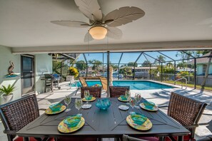 Uma área de refeições com uma mesa posta para seis pessoas, com vista para uma piscina e para o bairro.