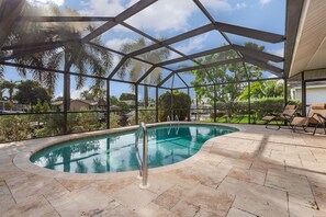 Piscina interior com cobertura de vidro, cercada por espreguiçadeiras e vista para palmeiras e casas.