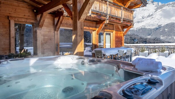 Une cabane en bois dotée d’un bain à remous, d’une terrasse en bois et offrant une vue sur des montagnes enneigées.