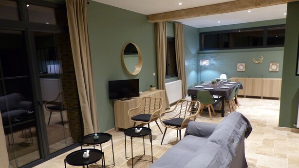 Ein modernes Wohnzimmer mit einer Couch, Sesseln, einem Fernseher und einem Essbereich mit Tisch und Stühlen.