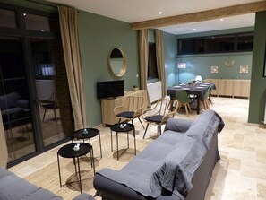 Uma sala de estar moderna com sofá, poltronas, televisão e área de refeições com mesa e cadeiras.