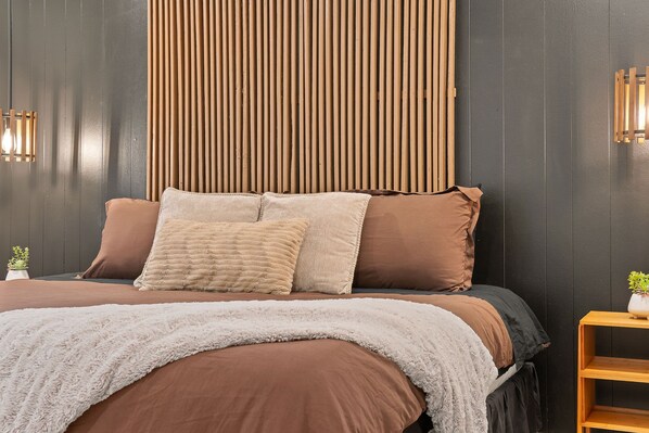 A bed with brown bedding, a white fluffy throw, and a wooden headboard.