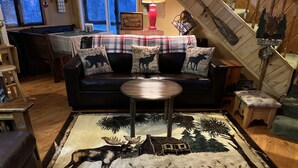 A cozy living room with a black sofa, a round coffee table, and a moose-themed rug.