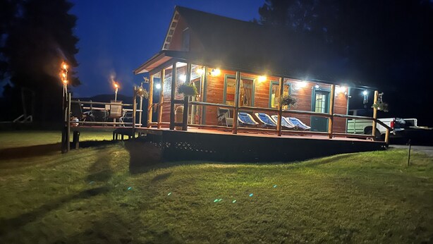 A wooden cabin with a covered deck, outdoor seating, and a swimming pool.