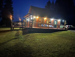 Una cabaña de madera con un porche cubierto, mobiliario exterior y una piscina.