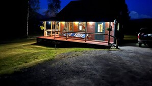 A wooden cabin with a deck and lounge chairs, surrounded by trees.