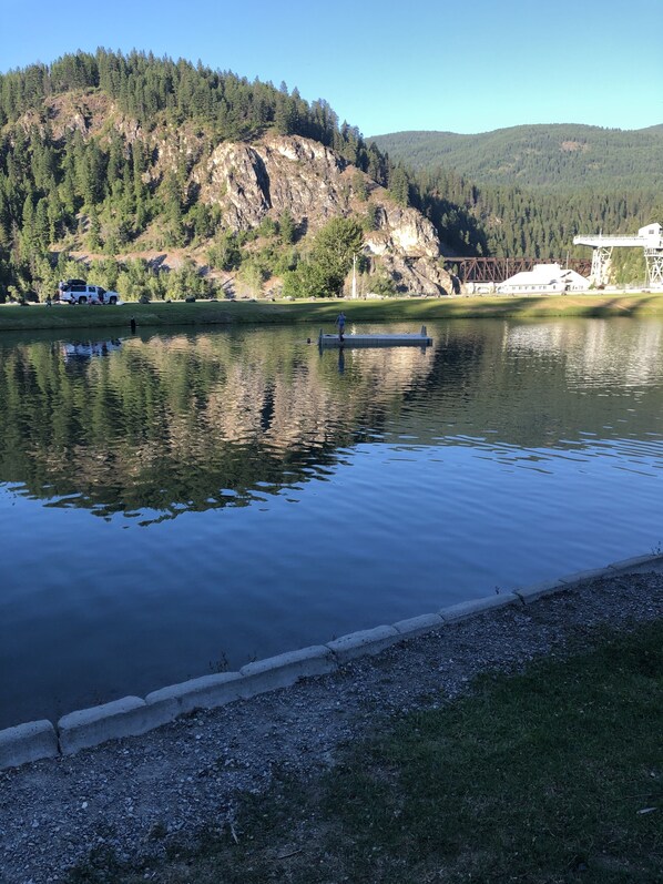 Un lago tranquilo con un muelle, rodeado de colinas boscosas y un cielo despejado.