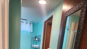 A narrow hallway with teal walls, wooden flooring, and a mirrored door. A metal shelf with towels is visible in the background.