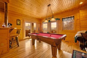 Un interior de madera con mesa de billar, zona de bar y sofá.