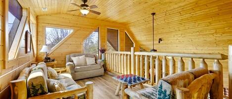 A wooden cabin interior with a sofa, a table, and a railing.