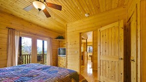 L'intérieur d'un chalet en bois, avec un lit, un téléviseur et un balcon.