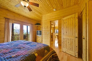 Interior de una cabaña de madera con una cama, un televisor y un balcón.