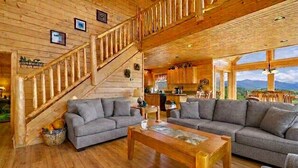 Un intérieur en bois avec un escalier, des canapés gris, une table basse en bois et un coin cuisine.