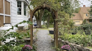 A pathway leading through a garden with a wooden archway, surrounded by greenery and potted plants.