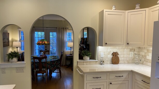 A kitchen with white cabinets, a tiled backsplash, and a dining area with a table and chairs.