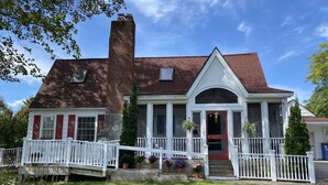 A two-story house with a white porch, red shutters, and a brick chimney.