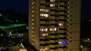 A multi-story hotel with illuminated windows and balconies, a parking area, and a small outdoor seating area.