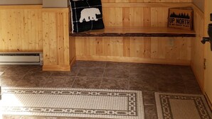 Interior de una cabaña de madera con un banco, un cartel de bienvenida, un cartel que dice 'Bienvenido al Bosque', un cartel que dice 'Ir al Norte es mi lugar feliz' y una guirnalda en la pared.