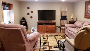 Una sala de estar con televisor, dos sofás, un tapete y un mueble de madera.