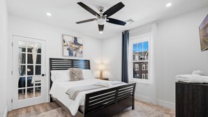 A bedroom with a bed, a ceiling fan, a window with a view, a door, and a nightstand with a lamp. - Renovated 2nd-Floor Home (Boston)