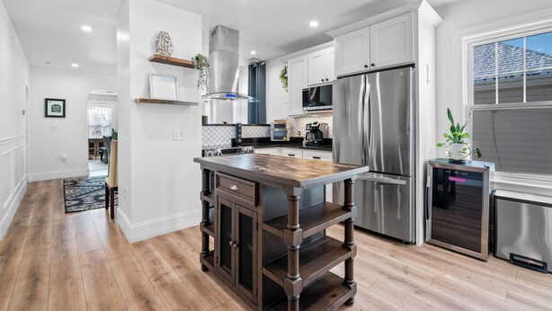 A modern kitchen with white cabinets, stainless steel appliances, and a wooden island. - Renovated 2nd-Floor Home (Boston)