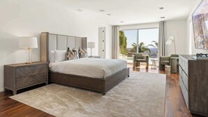A modern bedroom with a large bed, bedside tables, a desk, and a view of the outdoors. - Villa Lareira (Los Angeles)