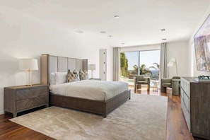 Un dormitorio moderno con una cama grande, mesitas de noche, un escritorio y vistas al exterior.