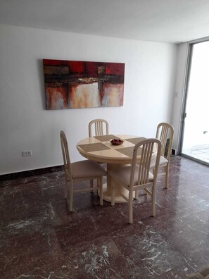 A dining area with a round table, four chairs, a painting on the wall, and a large window.