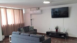 Un salon avec un canapé, un téléviseur à écran plat, un sol en marbre et une fenêtre avec des rideaux.