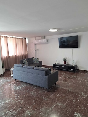 A living room with a sofa, a flat-screen TV, a marble floor, and a window with curtains.