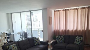 Un salon moderne avec deux canapés, une table basse et une grande fenêtre donnant sur des immeubles.