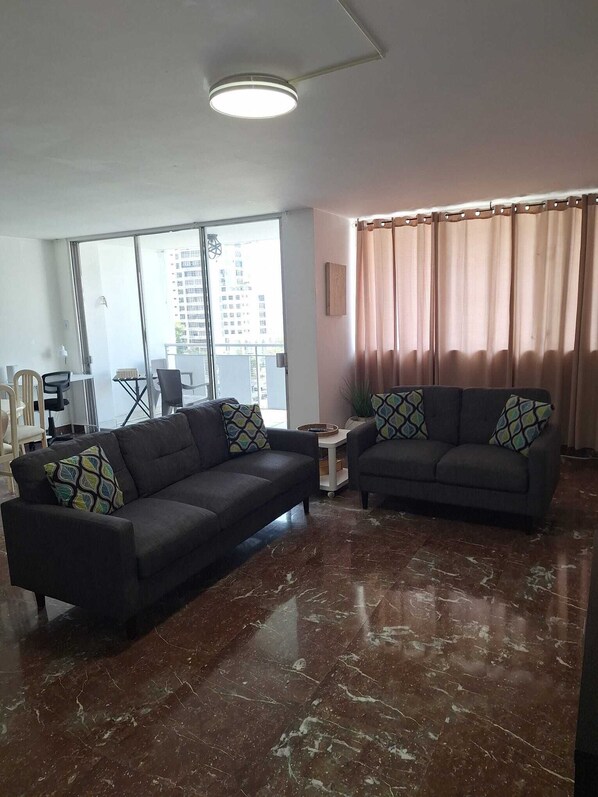 A modern living room with two sofas, a coffee table, and a large window with a view of buildings.