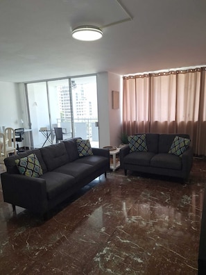 A modern living room with two sofas, a coffee table, and a large window with a view of buildings.