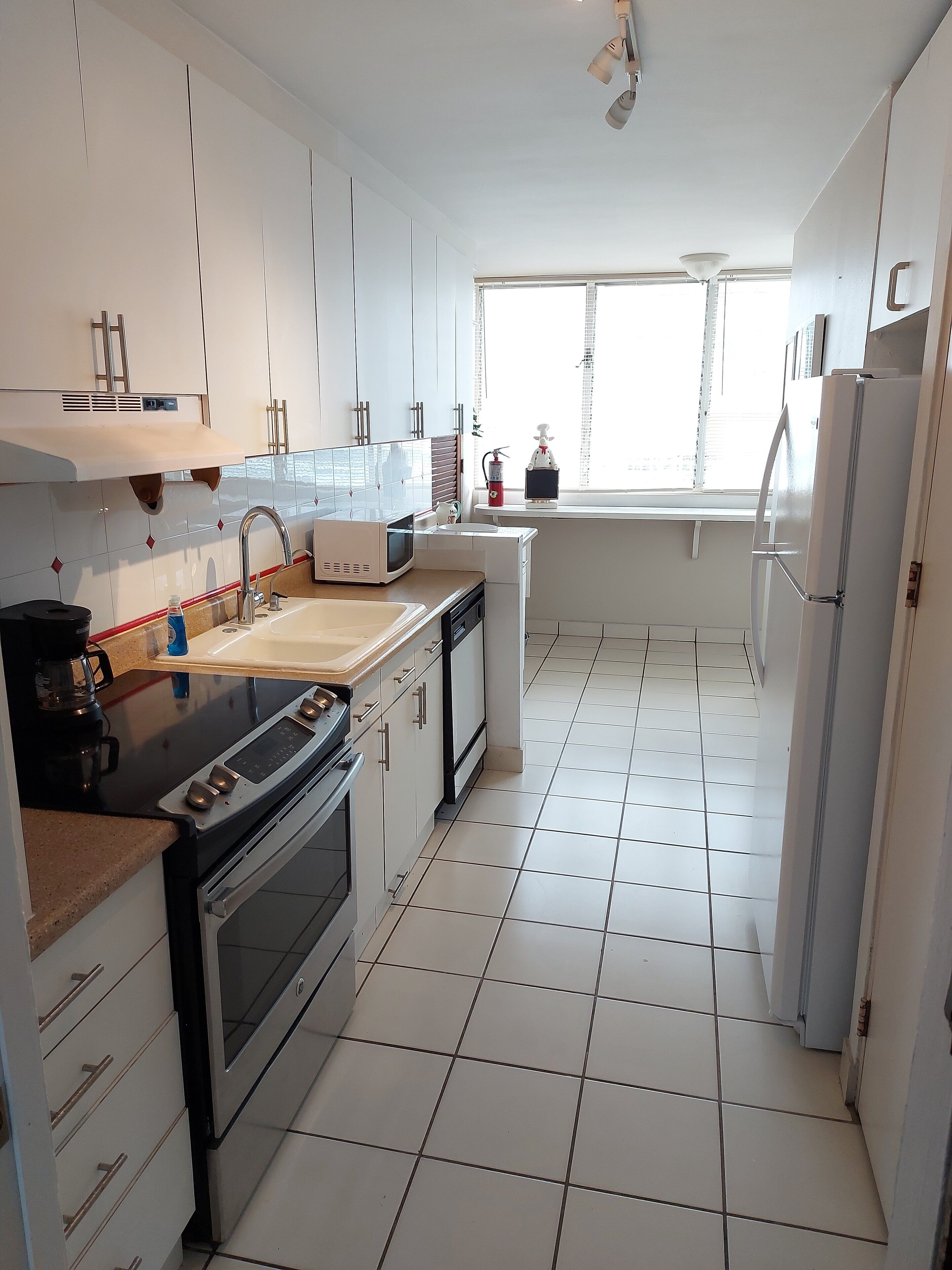 A modern kitchen with white cabinets, a stove, oven, microwave, and a sink.