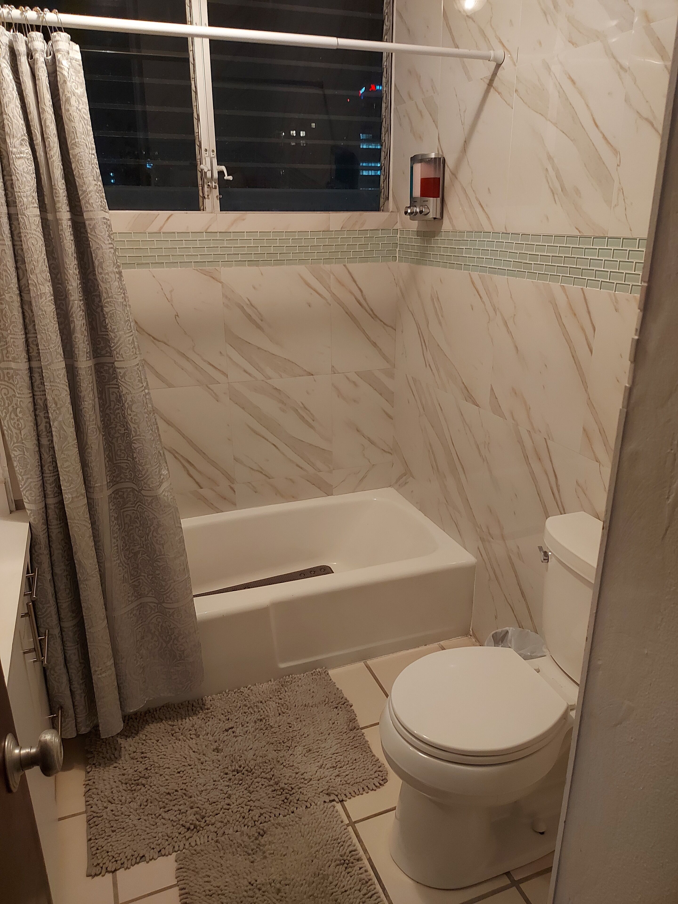 Une salle de bain avec une baignoire, des toilettes et une fenêtre avec des rideaux.