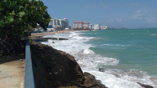 Une vue côtière avec un rivage rocheux, une plage et des bâtiments en arrière-plan.
