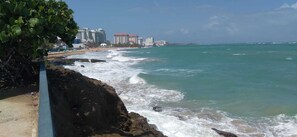 A coastal view with a rocky shoreline, a beach, and buildings in the background.