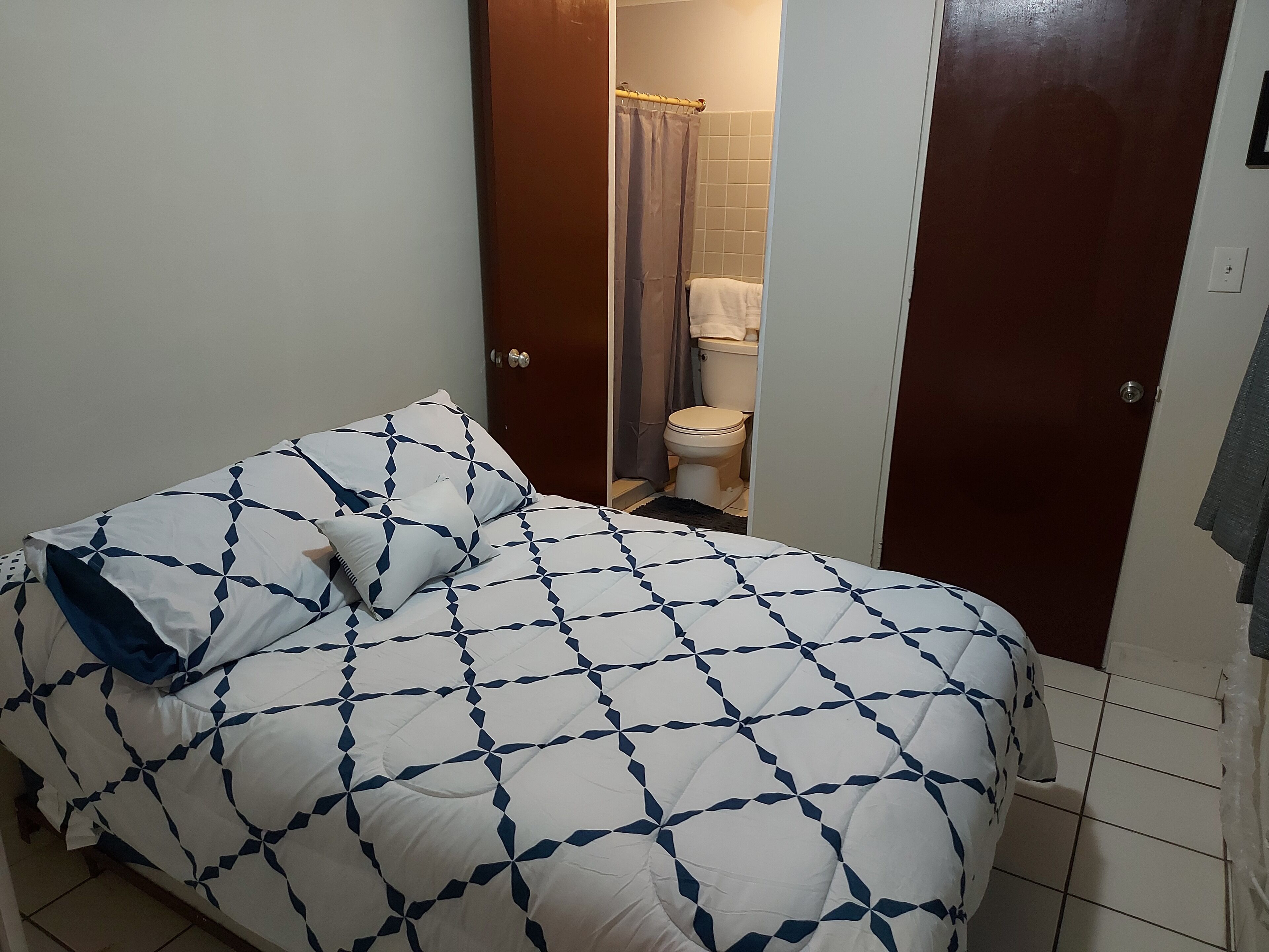 Un dormitorio con cama, un baño con inodoro y ducha, y una puerta que da a otra habitación.