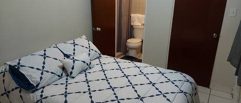 Un dormitorio con cama, un baño con inodoro y ducha, y una puerta que da a otra habitación.