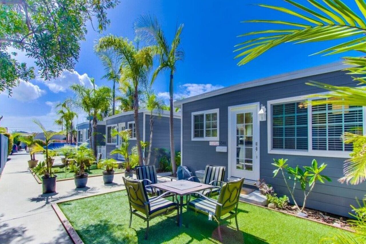 A modern two-story house with a patio area featuring a table and chairs, surrounded by potted plants and a well-maintained lawn.