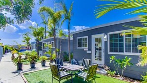 A modern two-story house with a patio area featuring a table and chairs, surrounded by potted plants and a well-maintained lawn. - Air Concierge Pacific Beach Breezy Cottages #3 (San Diego)