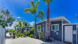 A row of modern, single-story buildings with a private driveway, surrounded by palm trees and greenery. - Air Concierge Pacific Beach Breezy Cottages #3 (San Diego)