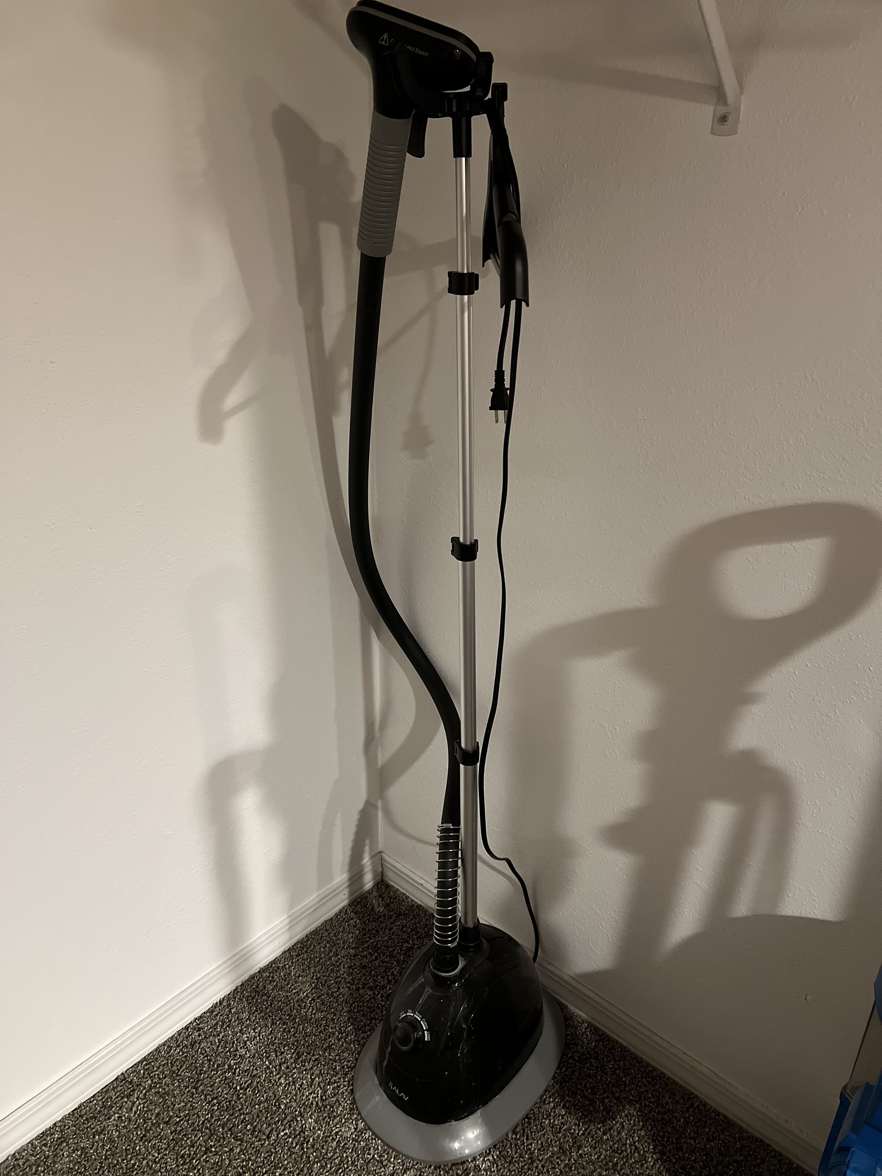 A standing exercise machine in a corner of a room with a white wall and carpeted floor.
