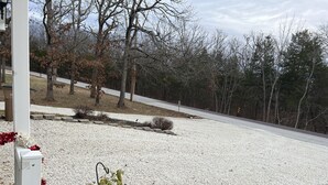 Uma entrada de automóvel residencial com superfície de cascalho, uma pequena área de jardim com plantas em vasos e uma rua ao fundo.
